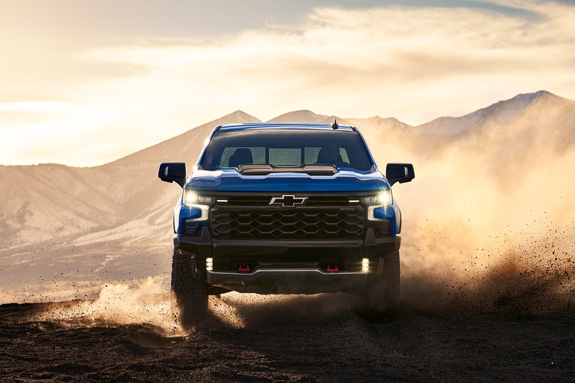 Card_Chevrolet Front view of 2025 Chevrolet Silverado ZR2 kicking up dust off-road at sunset with mountains in background.