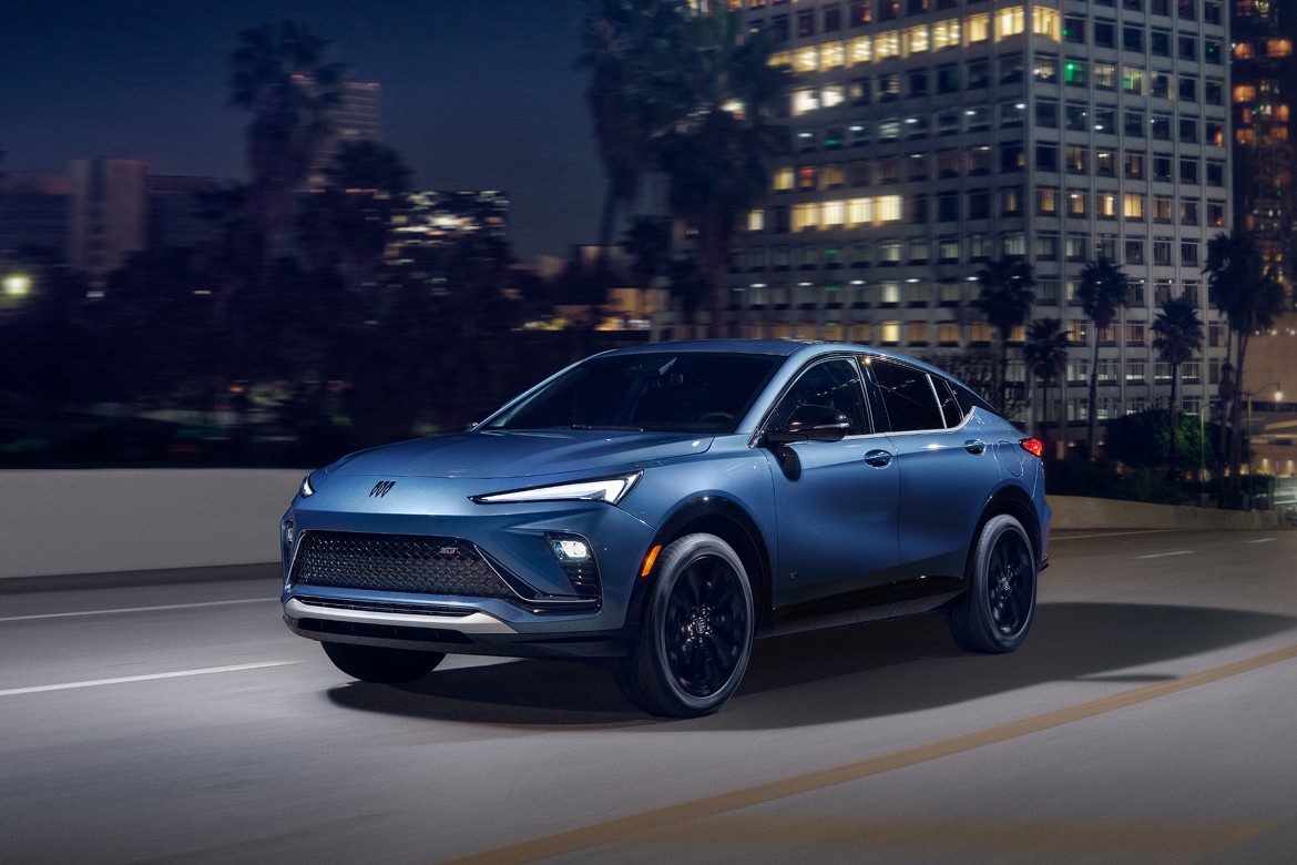 Card_Buick Sleek blue metallic 2025 Buick Envista driving on highway at night with palm trees and buildings in background.