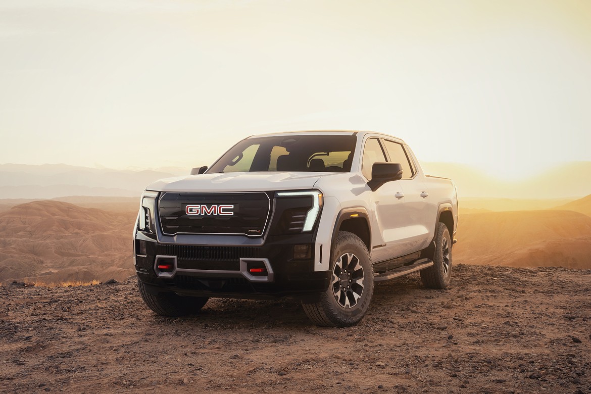 Card_GMC 2026 GMC Sierra EV Denali at sunset, front three-quarter view in open landscape with signature LED lighting.