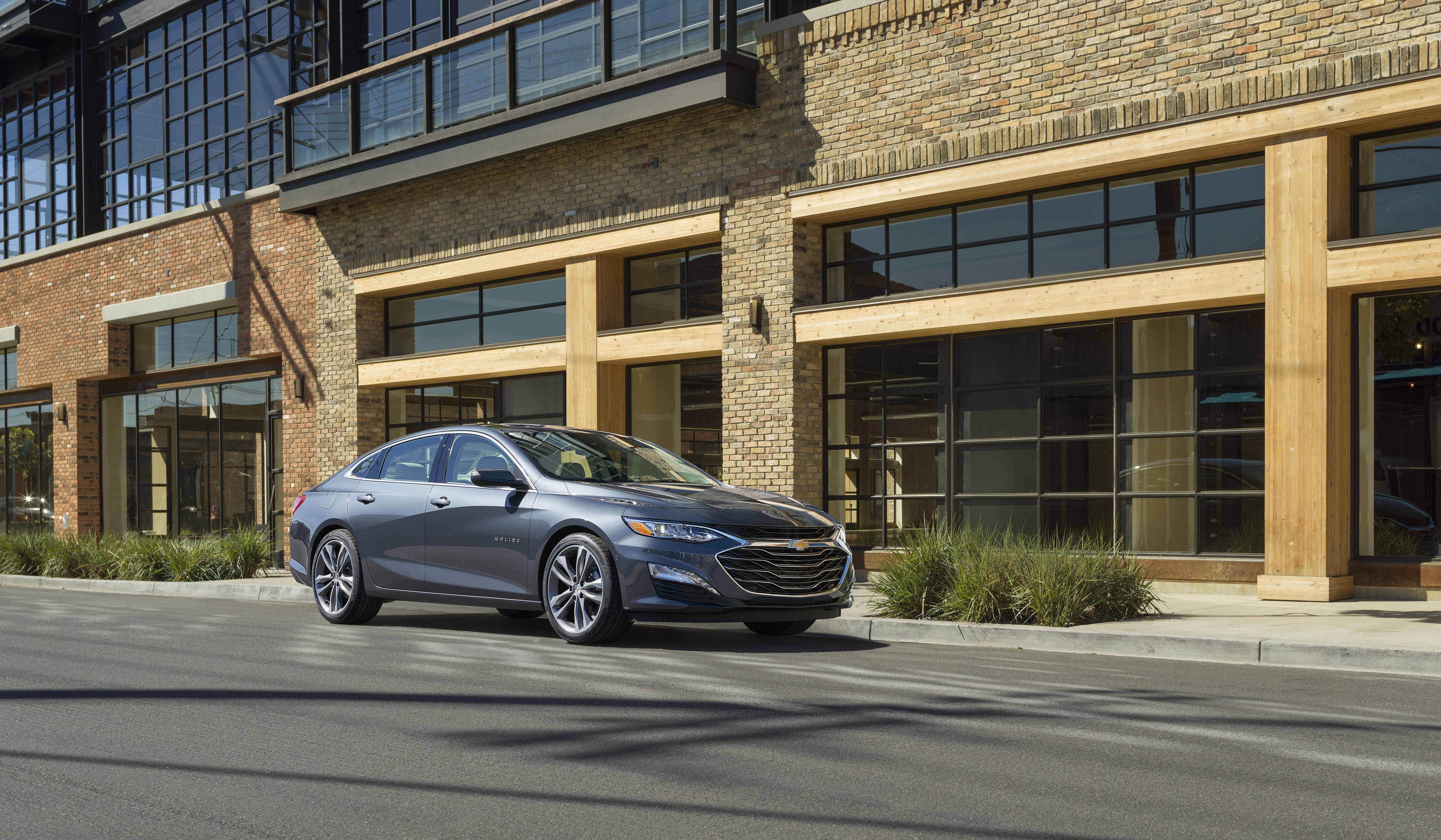 Front side view of 2021 Chevrolet Malibu driving in front of modern commercial building