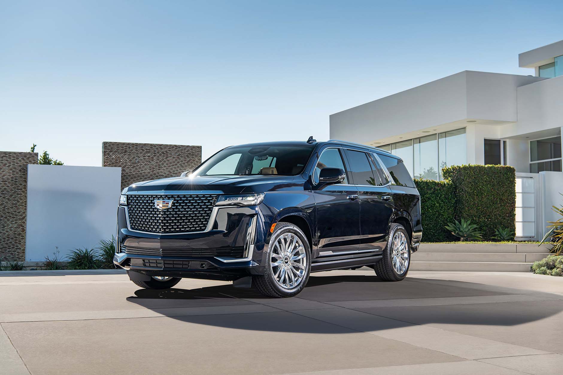 Front / side view of dark colored 2021 Cadillac Escalade parked in driveway in front of modern white house