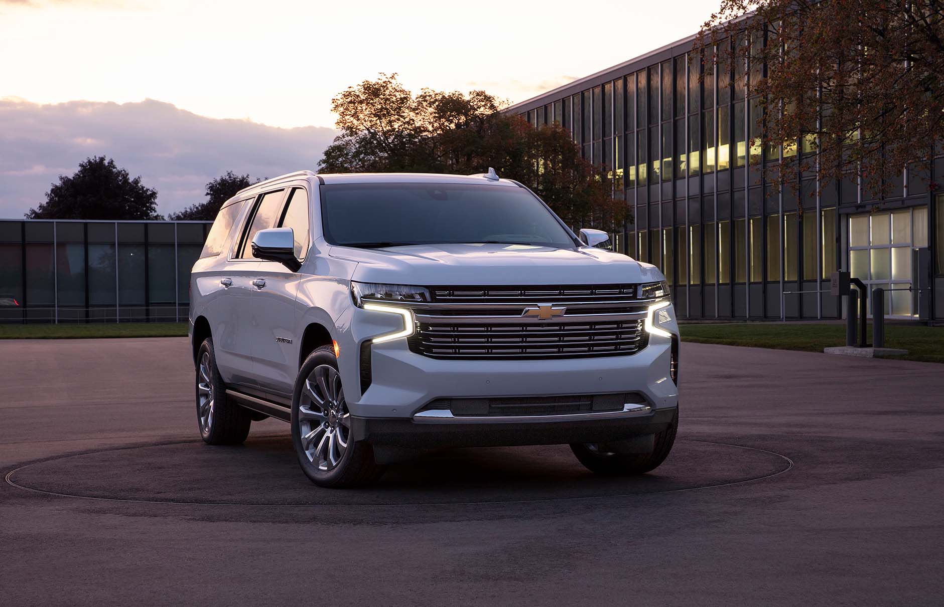 Front / side view of white 2021 Chevrolet Suburban parked in parking lot of modern office building