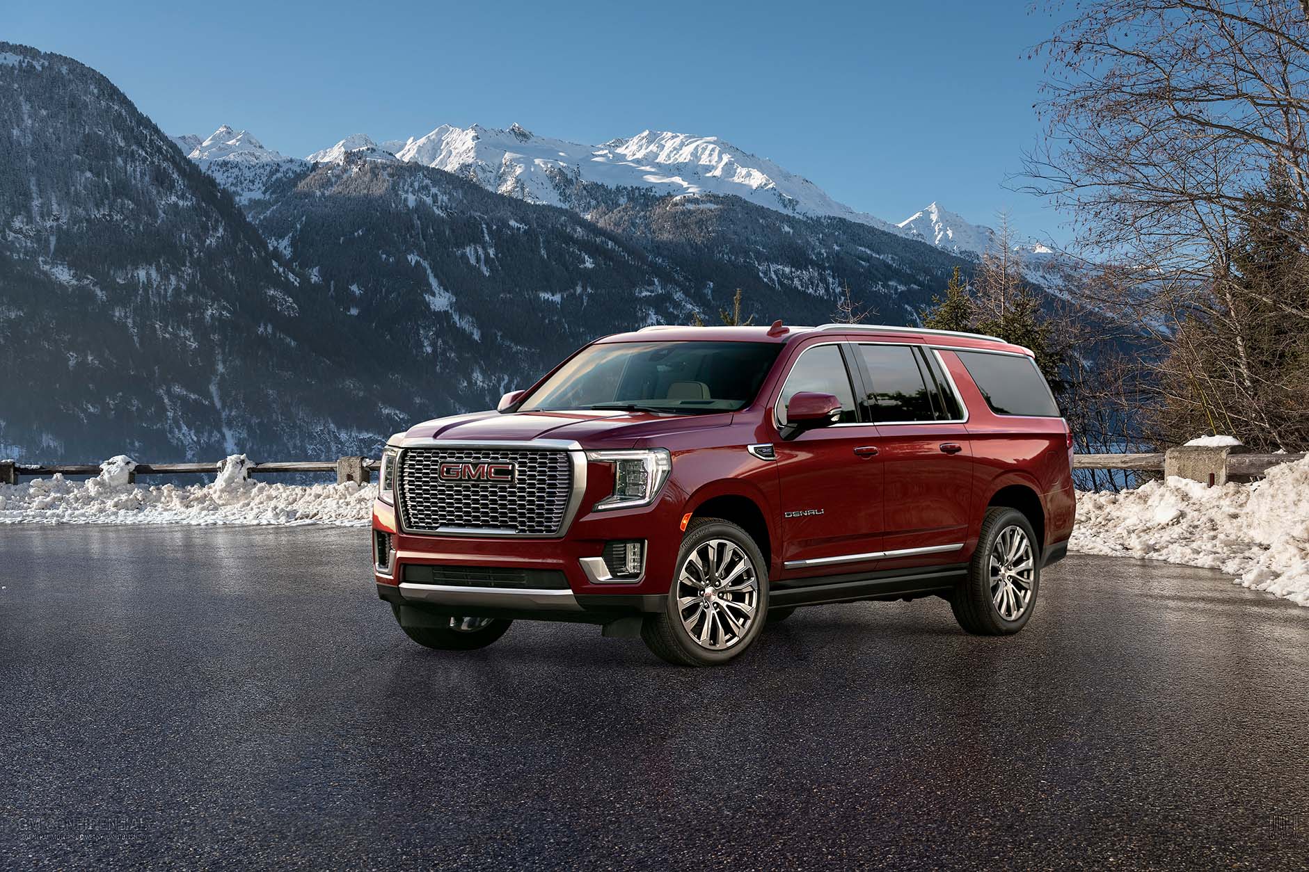 Front and side view of red 2021 GMC Yukon XL Denali parked in asphalt parking lot with snow on ground and on mountain peaks in the background