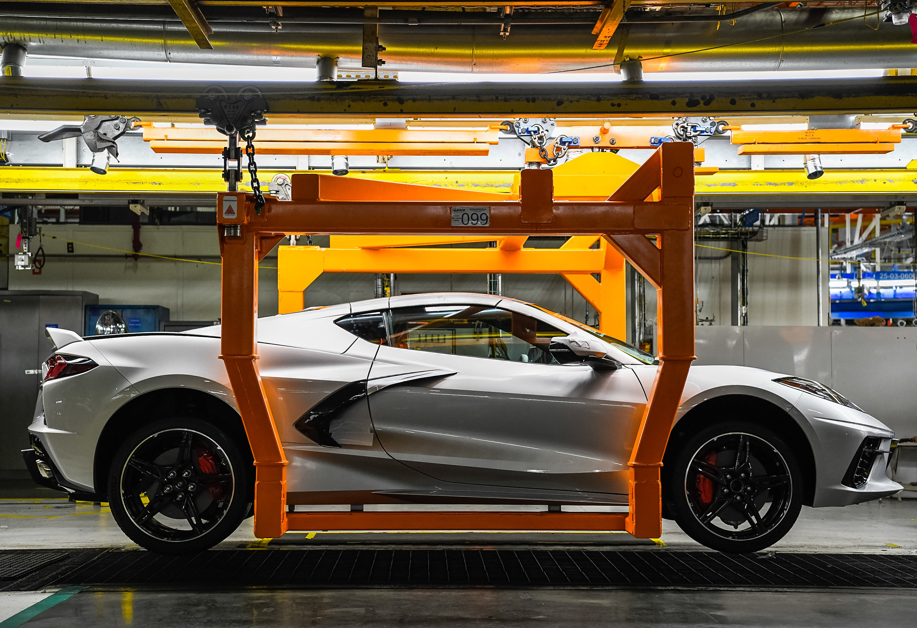 Side view of white corvette being moved down assembly line with lift 