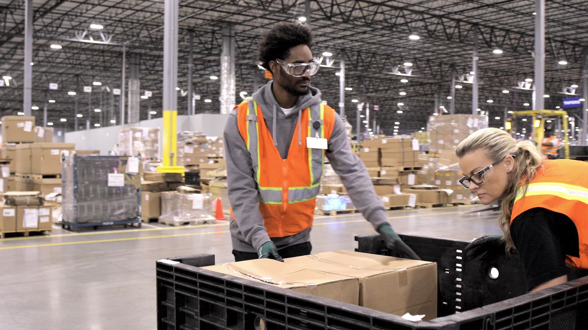 Two workers place completed packed cardboard boxes in plastic bin