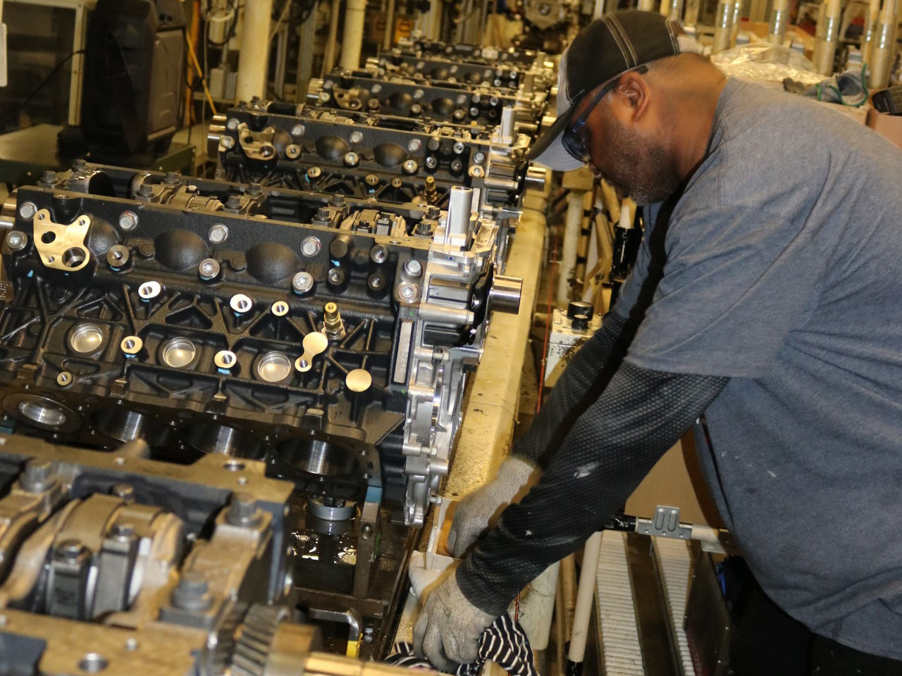 A worker works on one of several Duramax diesel engines moving down assembly line