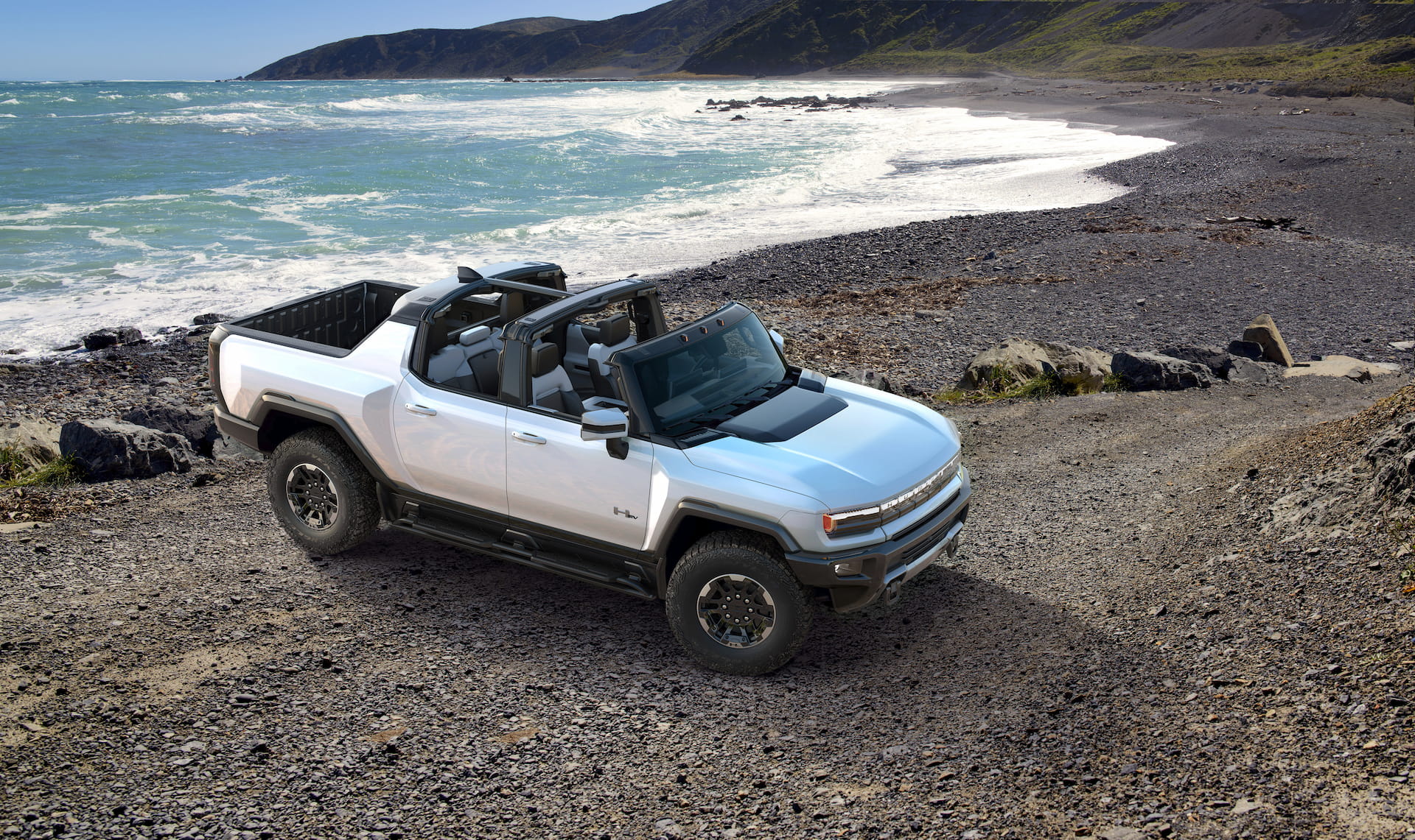White 2022 GMC HUMMER EV with top removed parked on rocky beach with white cap waves crashing in background