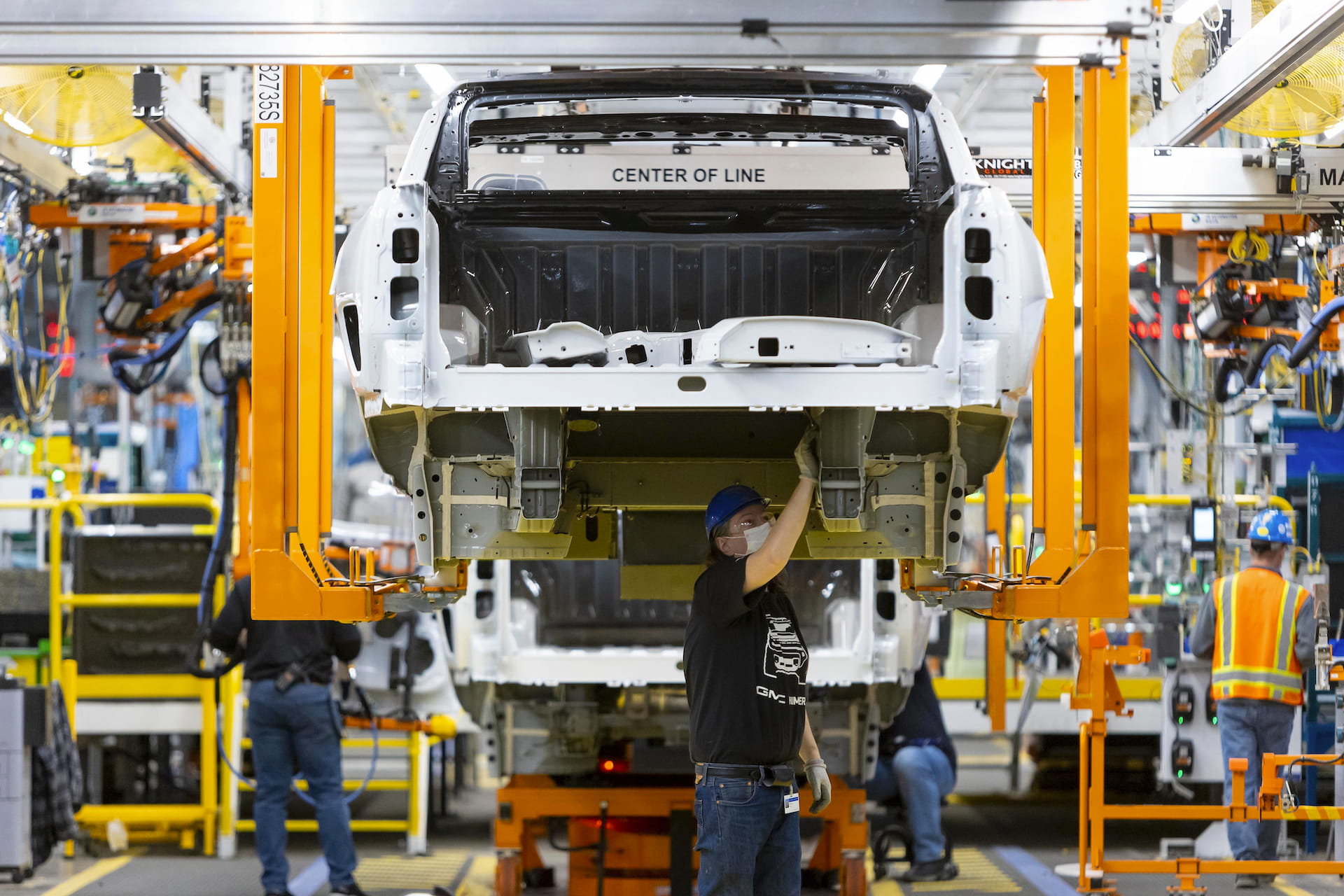 Assembly line worker works underneath  partially assembled Hummer EV