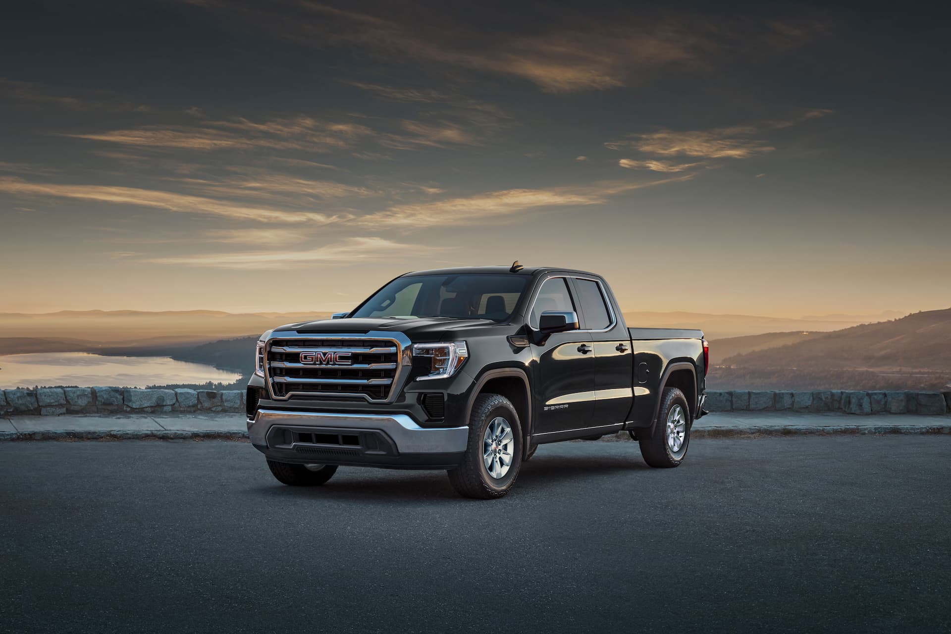 Front and side view of 2021 GMC Sierra with sun setting behind hills in the background