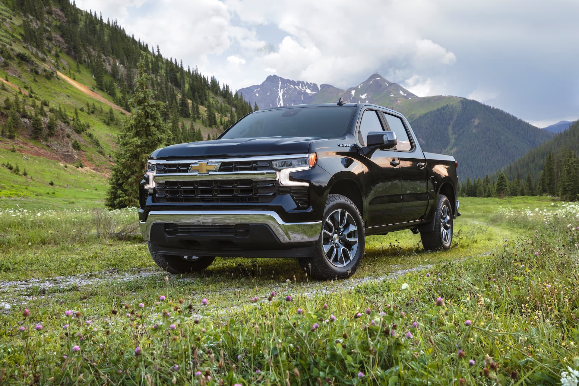 Front and side view of 2022 Chevrolet Silverado LT on grass covered road with tree covered hills and mountains in background