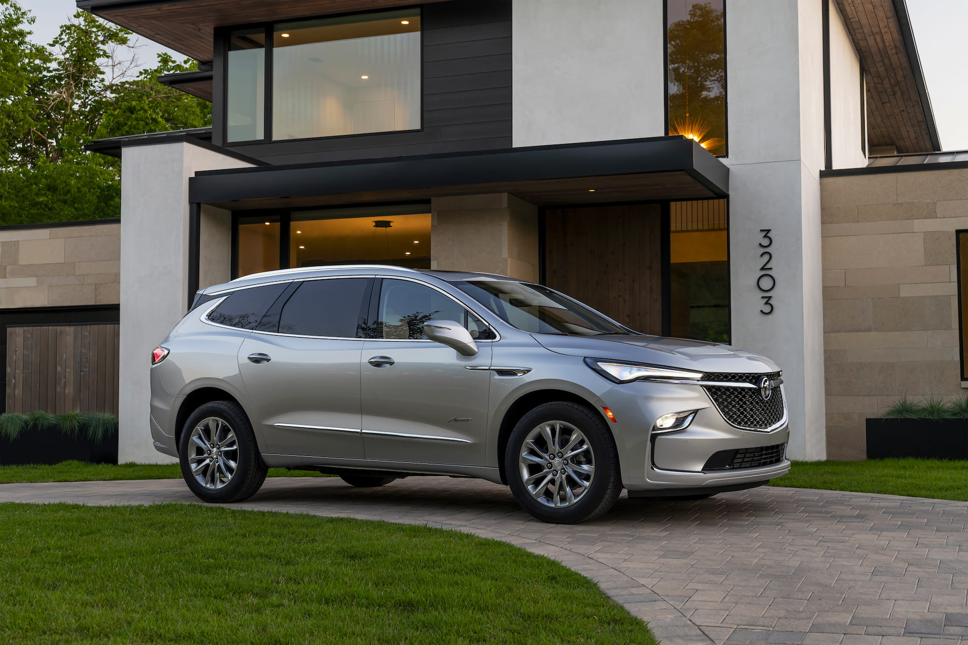 Side view of silver 2022 Buick Enclave Avenir parked in a driveway in front of modern home