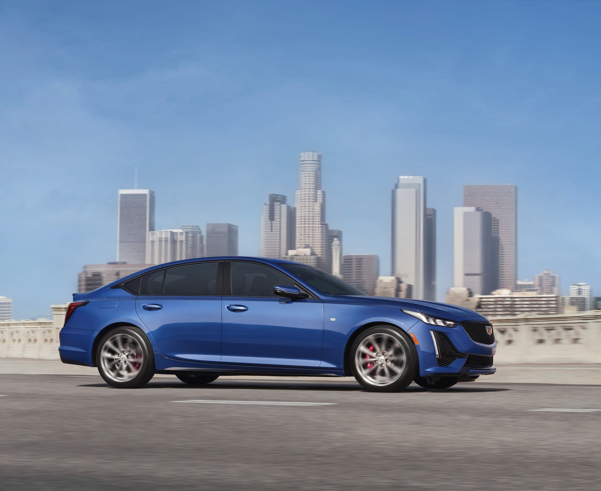 Side view of blue 2021 Cadillac CT5 on road with city sky line in background 
