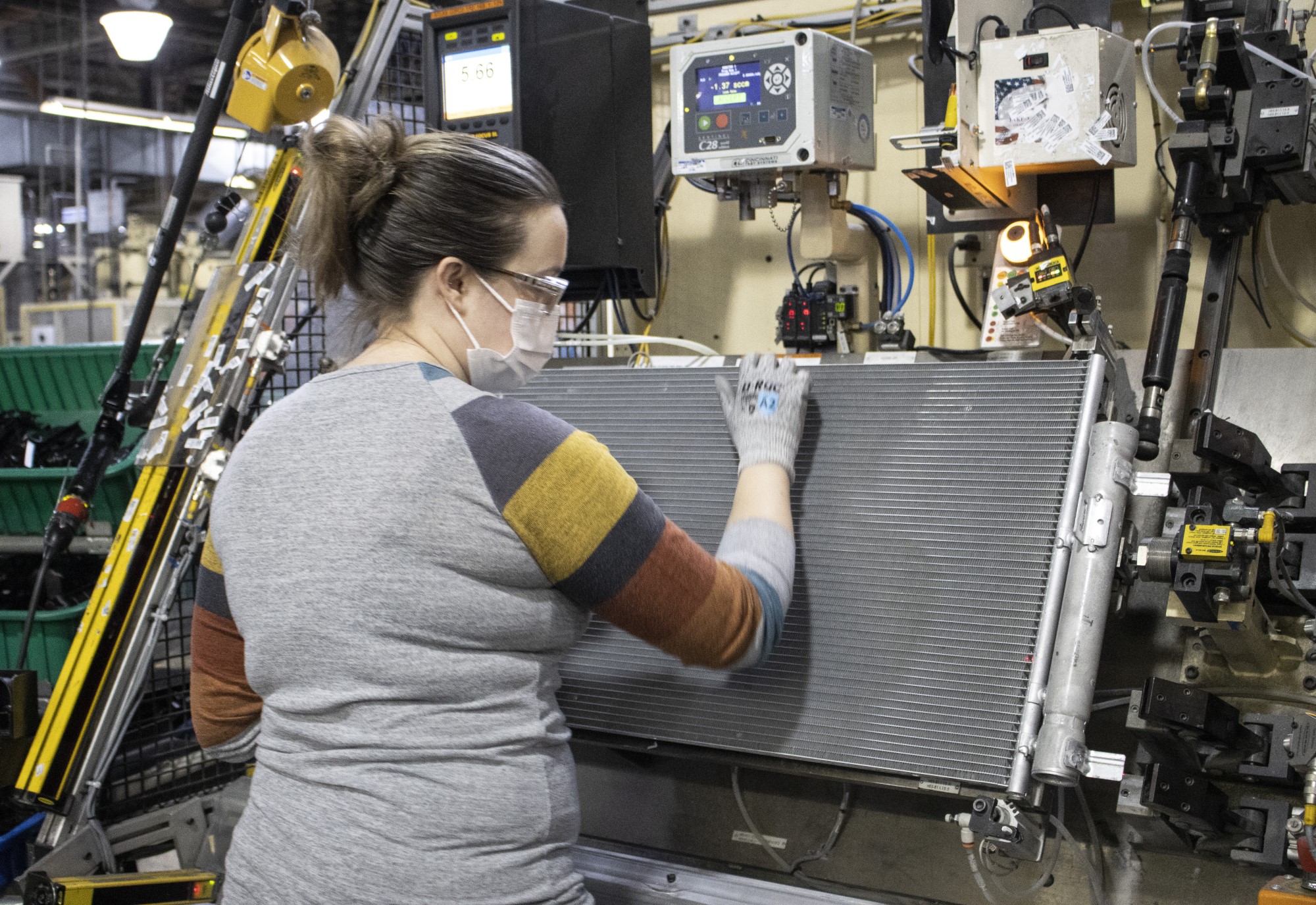 worker in PPE works with flat metal panel surrounded by production machinery