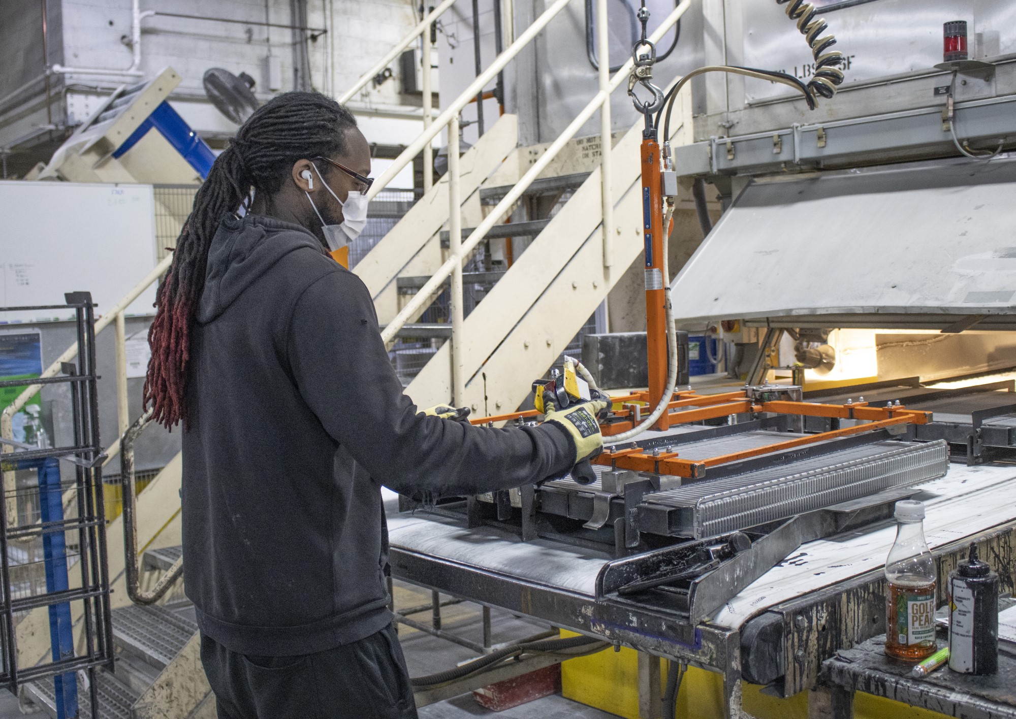 worker in PPE uses hand tool to work on large metal block component on table 