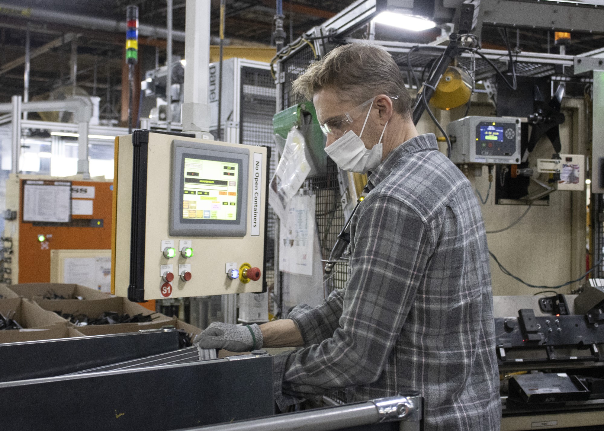 worker in PPE moves parts on to assembly line with equipment status computer screen in front of him