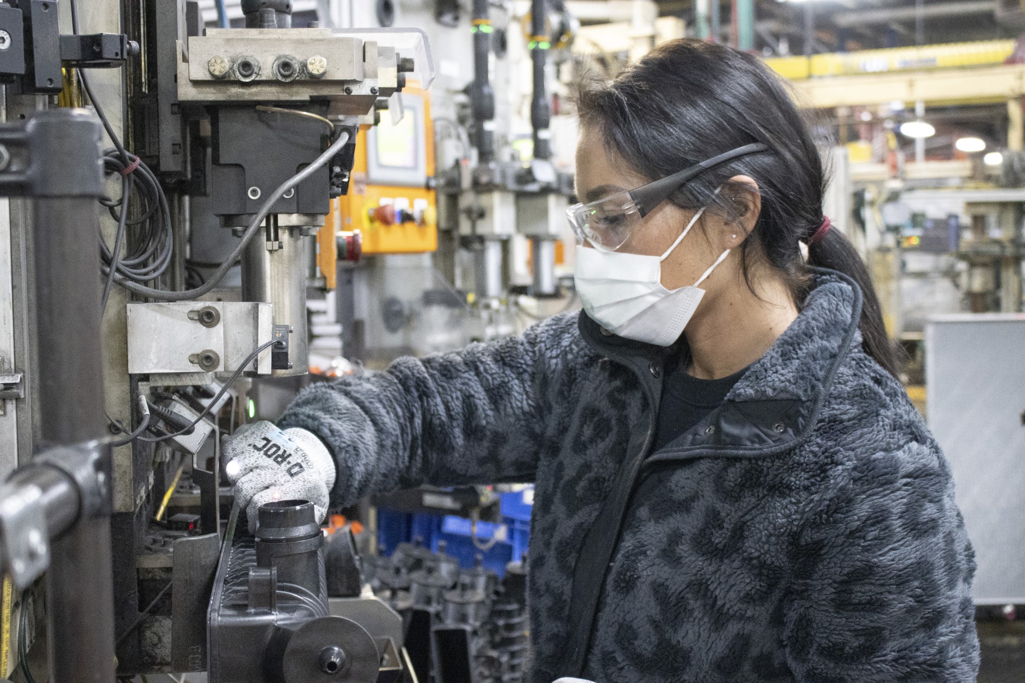 worker in PPE places small parts into large crimping machine in front of her
