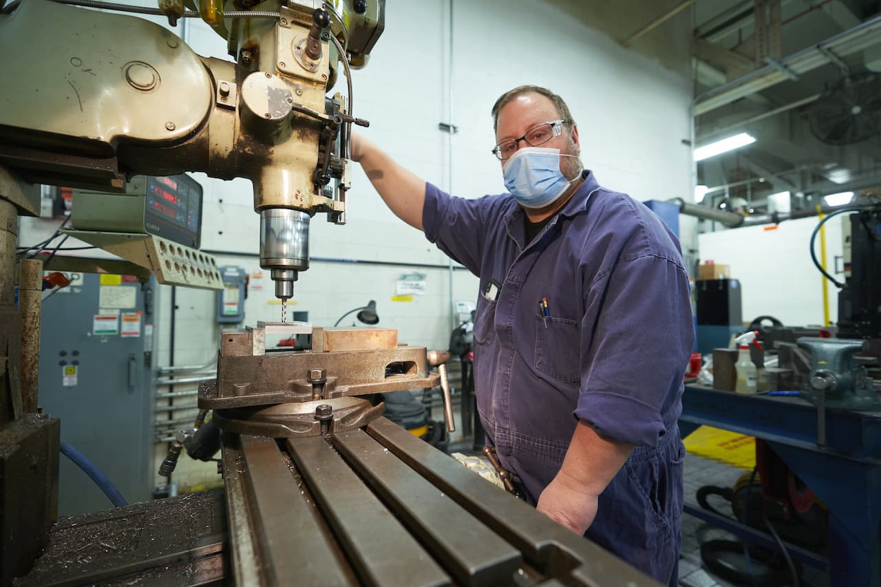 Worker uses drill press on sheet metal parts