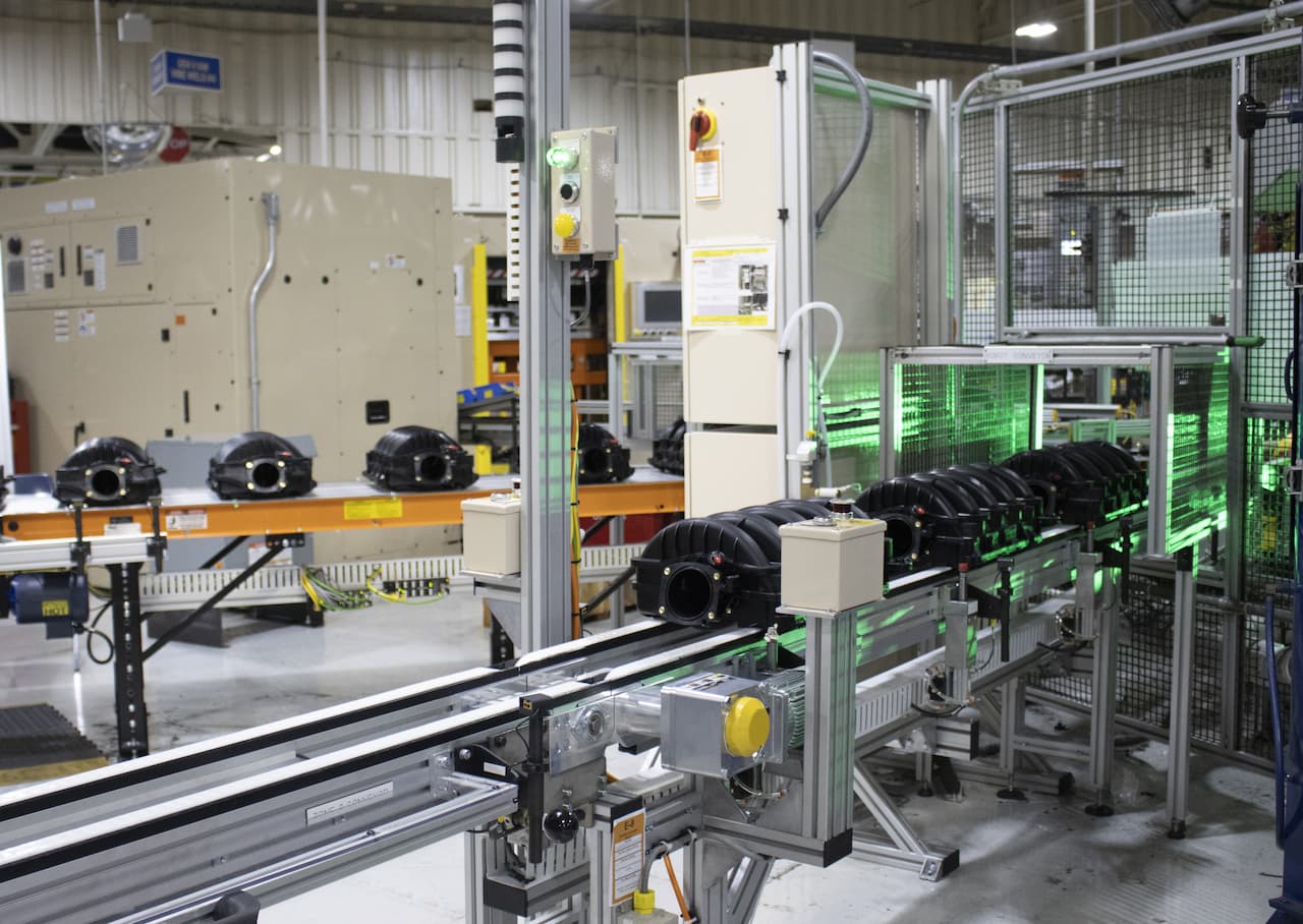 series of sub assembly parts move down conveyor and through caged area for additional work