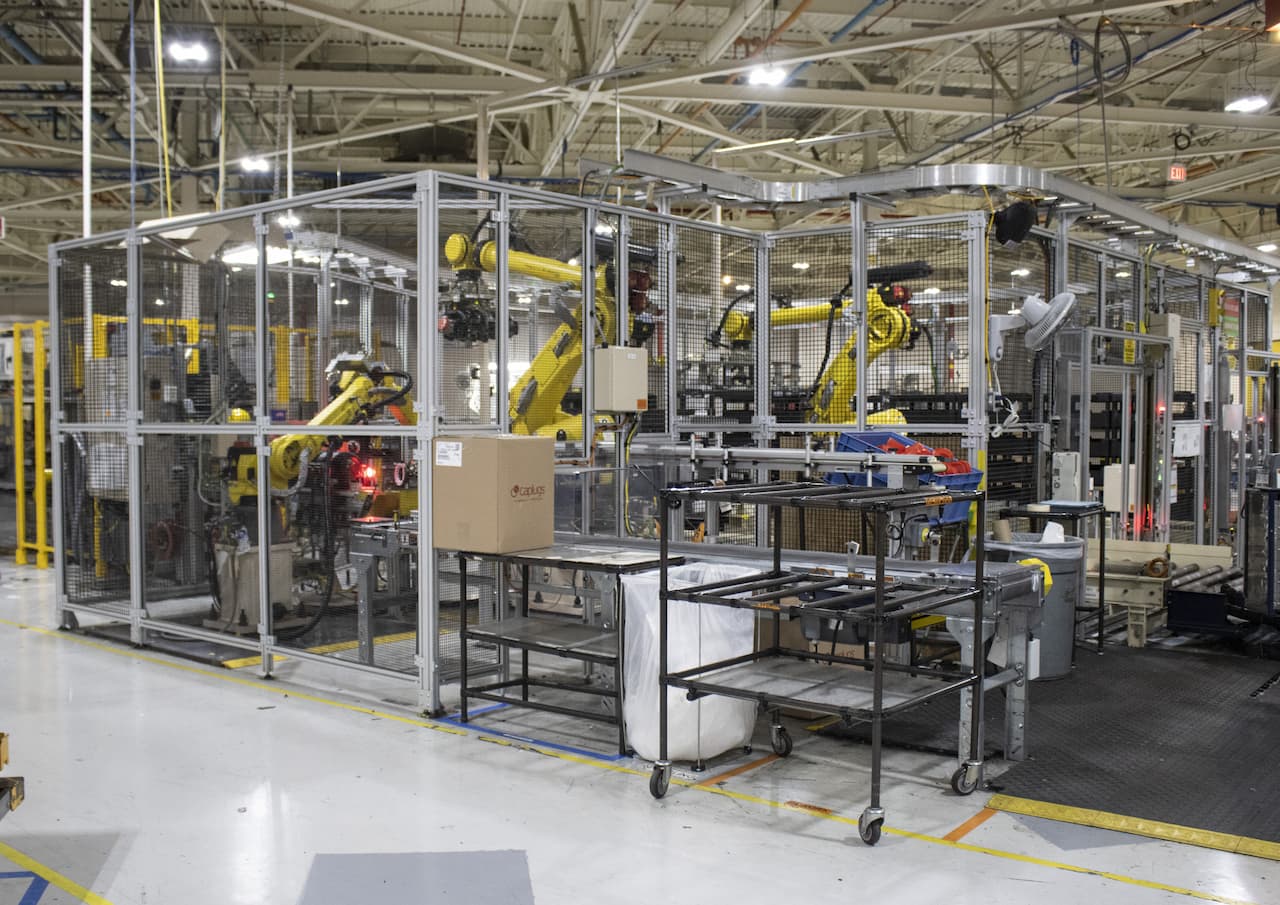three large yellow robotic arms work inside protective cage on Rochestor Operations plant floor