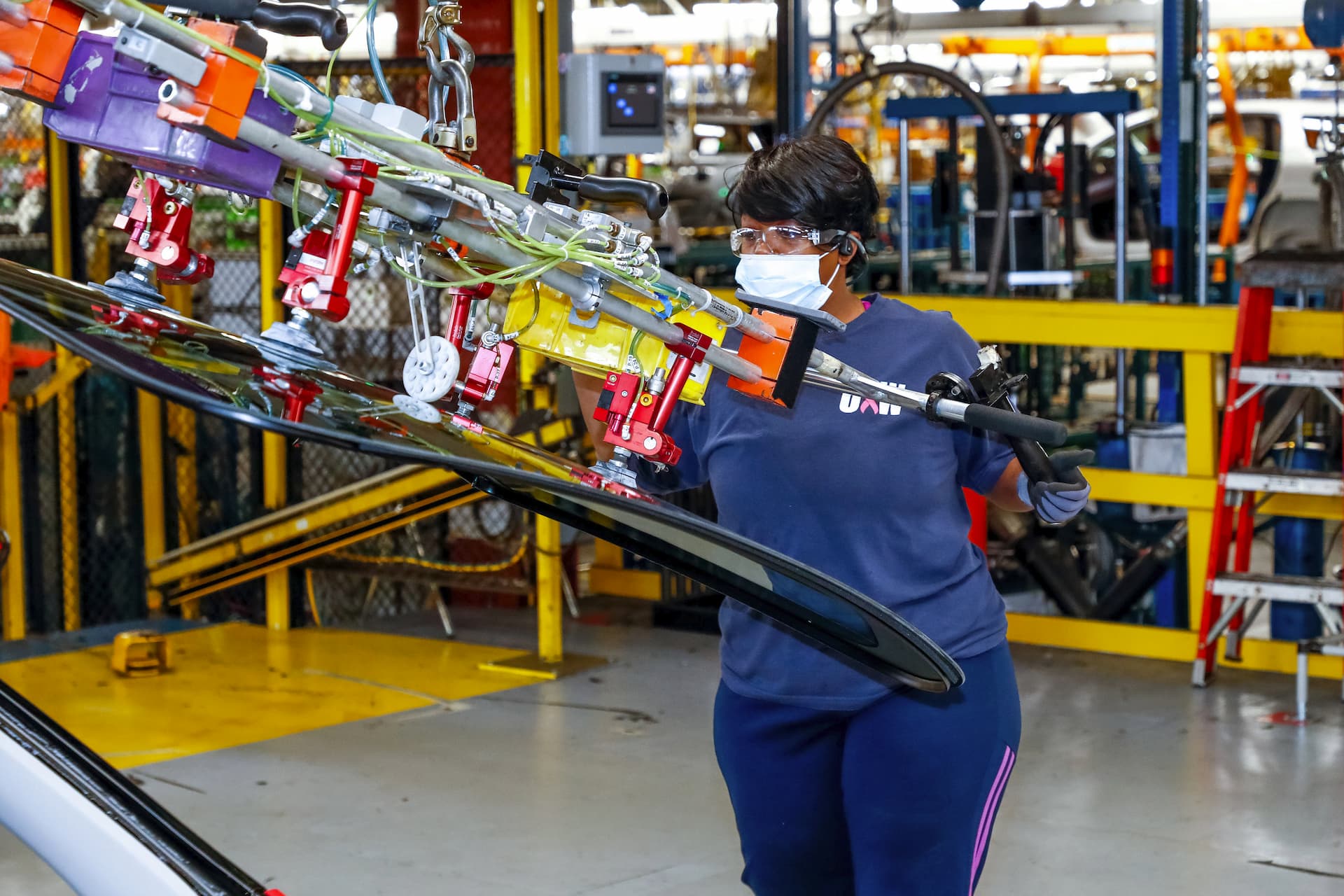 Assembly line worker uses tool to move windshield into place to put on new vehicle
