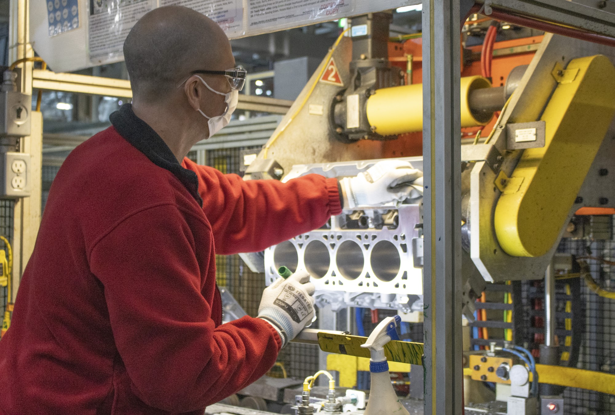 lift holds engine block up in well lit area as worker does detailed work on it
