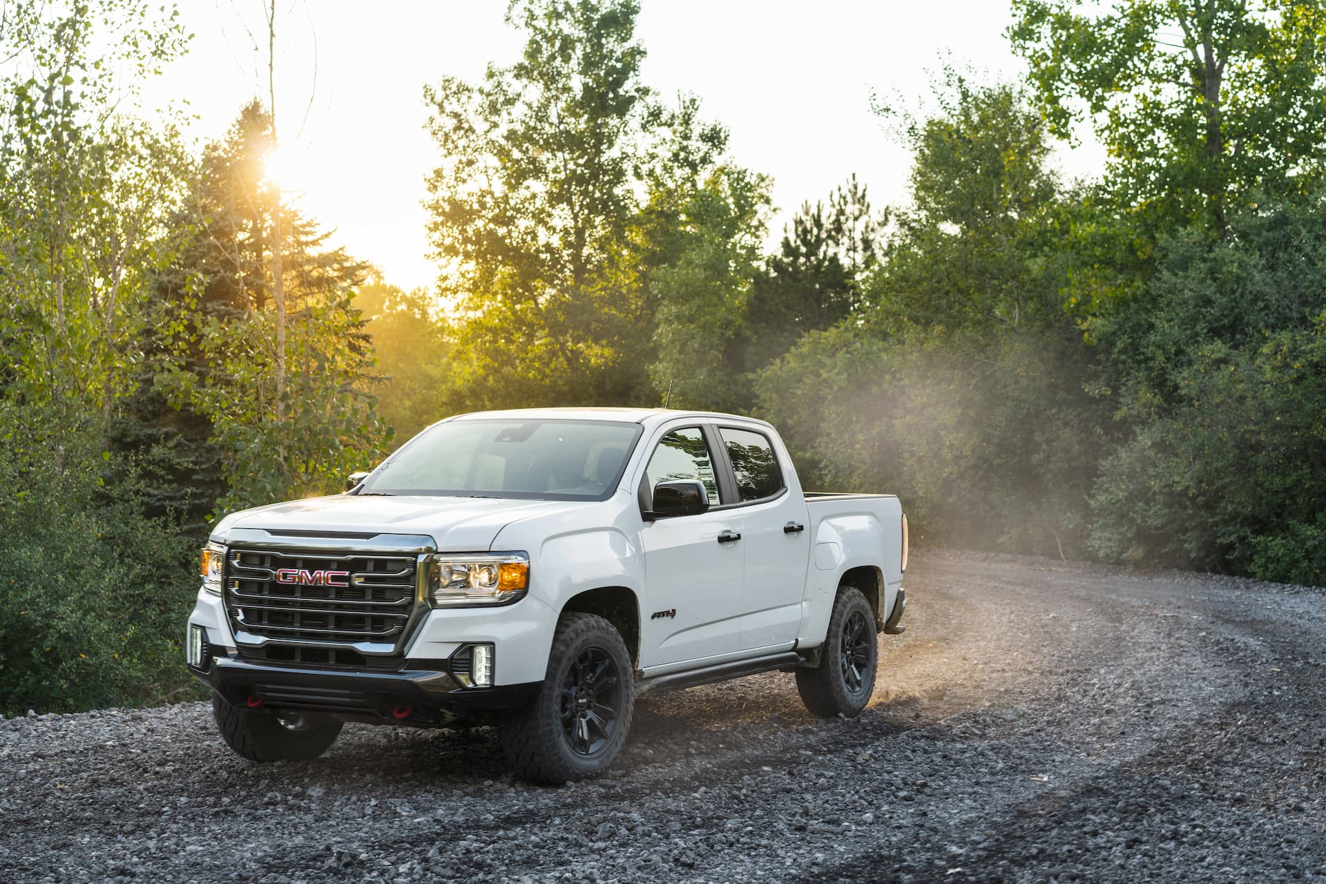 White 2021 GMC Canyon AT4 Off-Road Performance Edition drives down gravel road In wooded area