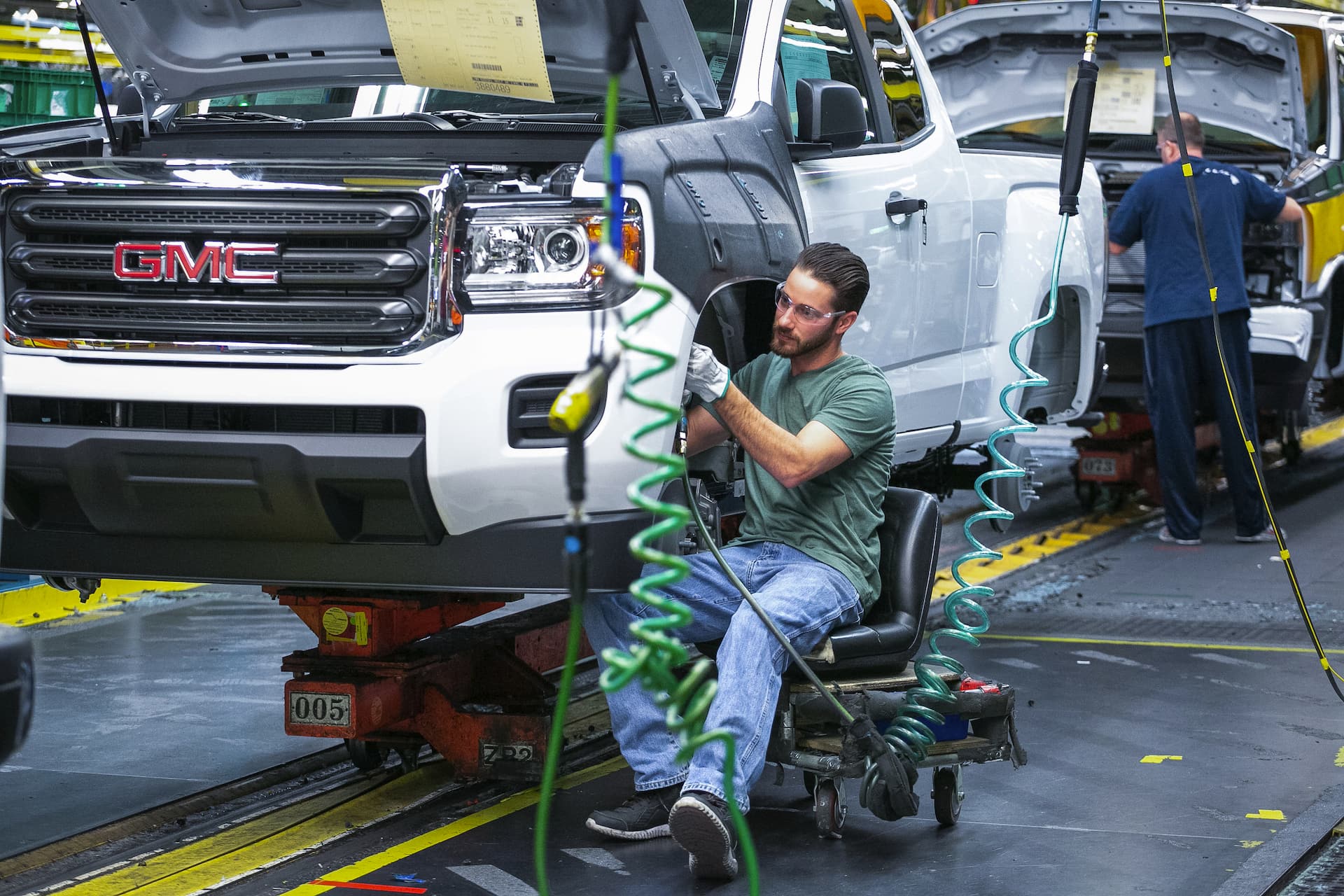 Assembly line worker works under front left wheel well of 2021 GMC Canyon undergoing assembly