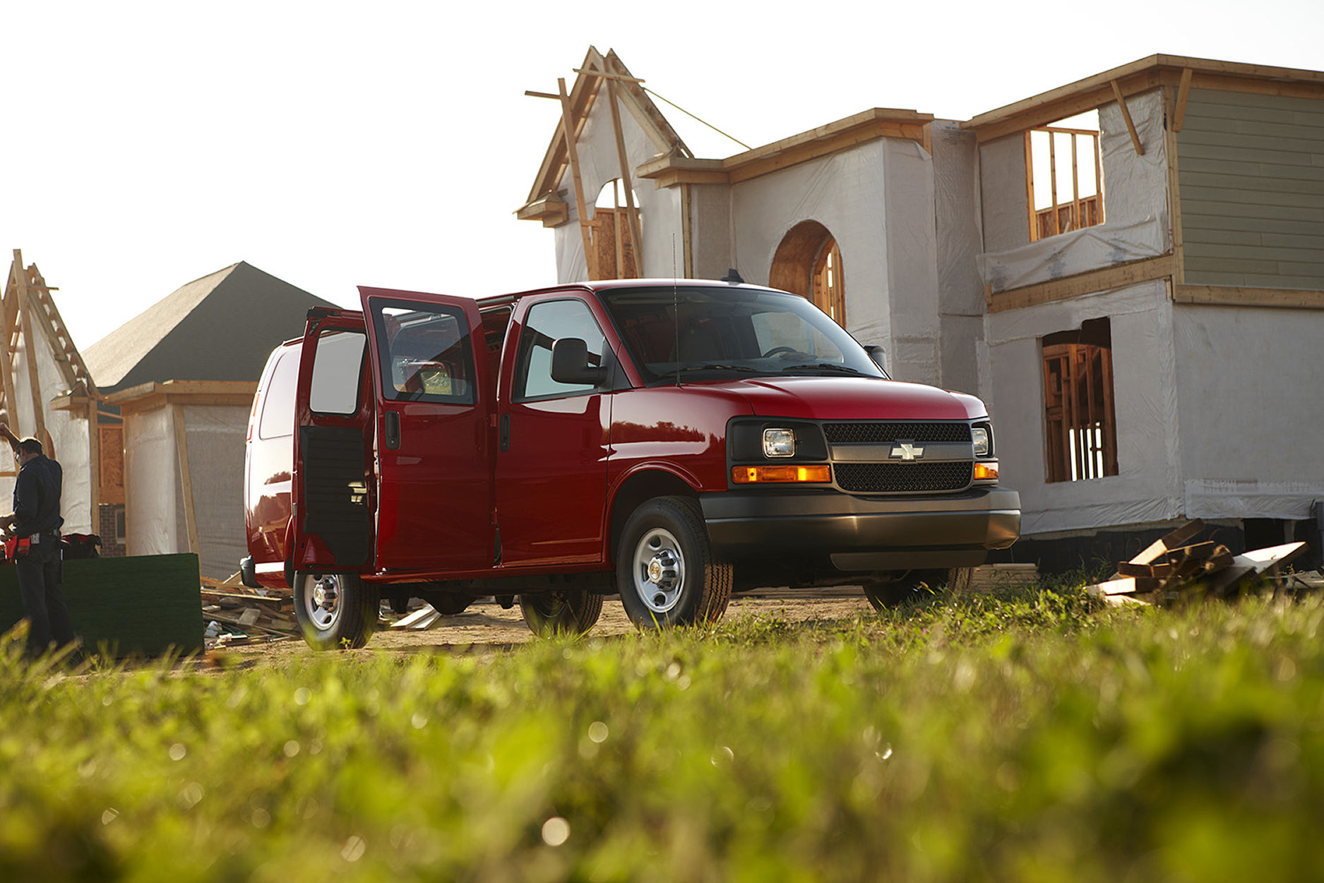 Front / side view of red express van with side doors open parked In front of home under construction