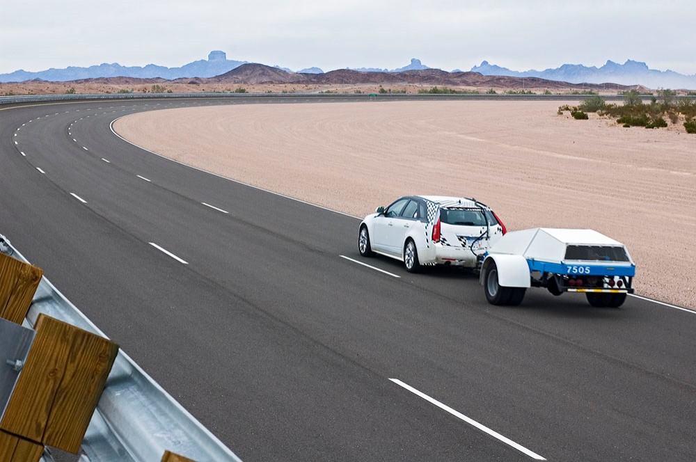 Cadillac car towing a trailer on the three lane, 3.5-mile Yuma Desert Proving Ground circle test track.