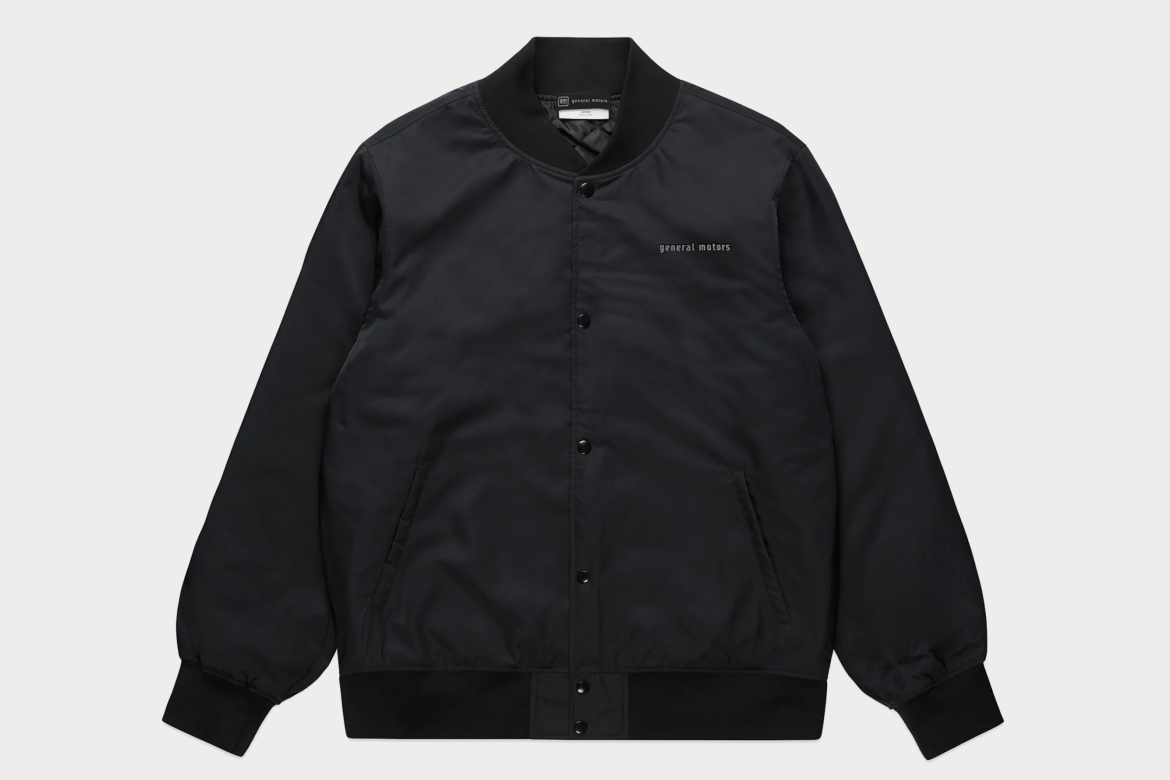 Black Collegiate Bomber Jacket With General Motors Text on Chest. It Has Button-Up Front, Side Pickets, and Ribbed Cuffs