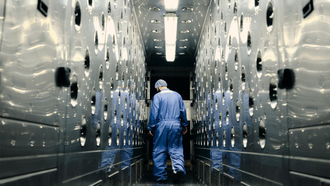 innovation A GM Technician in a Full-body Suit and Hairnet in a Brightly Lit Lab Lined with Circular Indentations on Both Sides