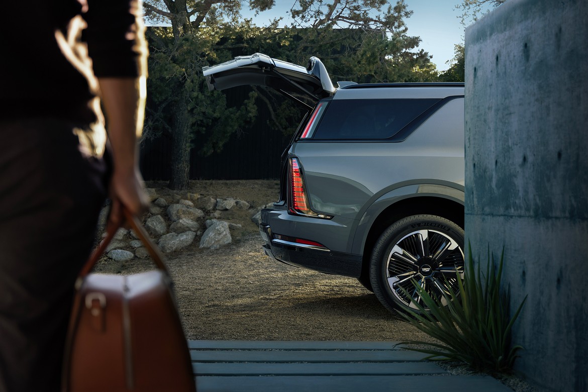 2026 Cadillac Escalade IQ rear view with open liftgate, parked outdoors as person approaches with brown leather travel bag.