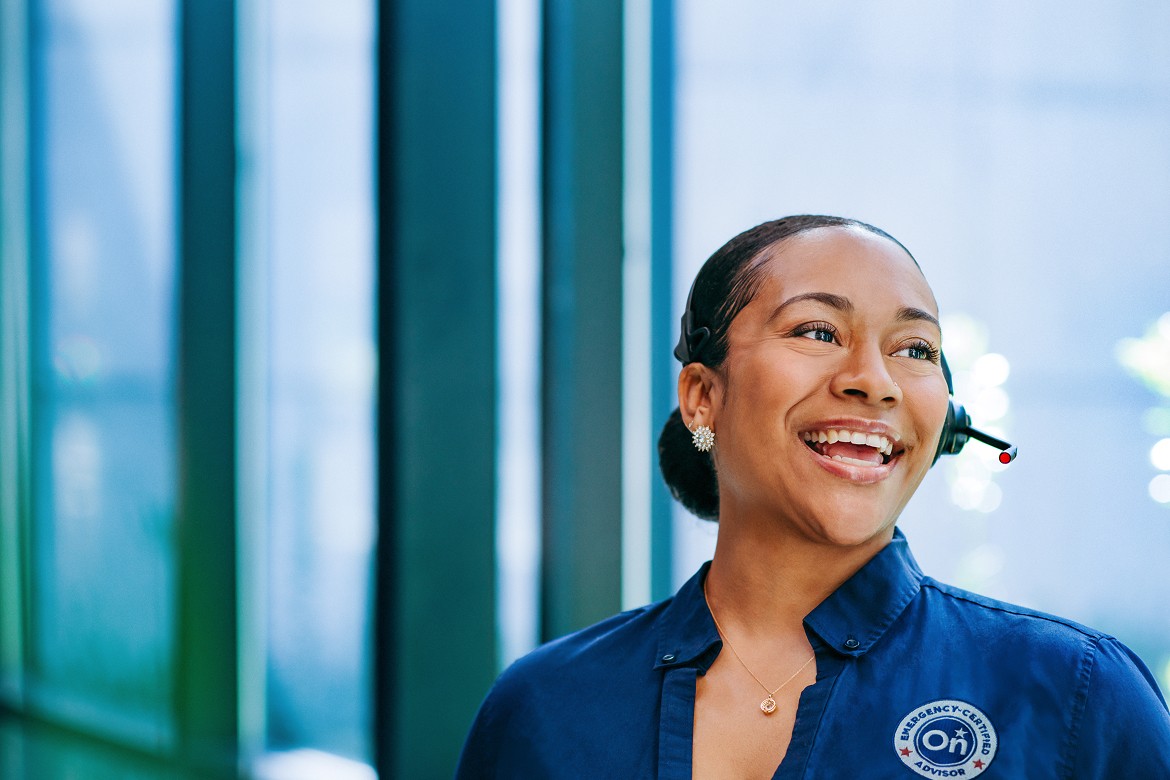 Smiling OnStar Emergency-Certified Advisor wearing a headset and navy uniform stands in a brightly lit modern office.